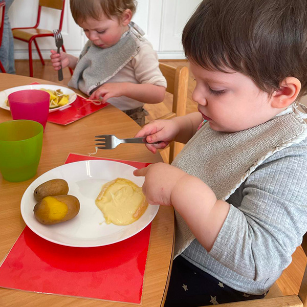 Un enfant découvre la raclette, concentré sur son assiette de pommes de terre et fromage fondu.