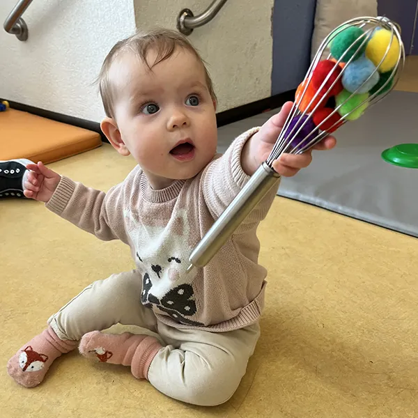 Un bébé tente d’attraper un pompon coincé dans un fouet à la crèche Les Petits Acrobates à Lausanne.