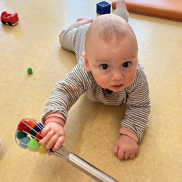 Un bébé tente d’attraper un pompon coincé dans un fouet à la crèche Les Petits Acrobates à Lausanne.