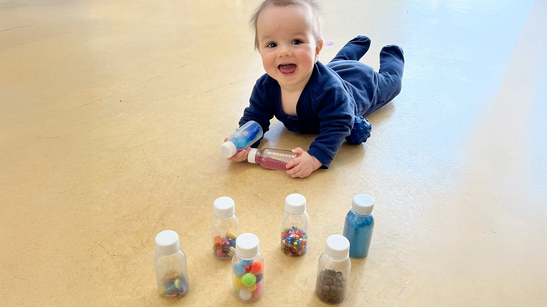 Bébé allongé sur le ventre observant une quille sensorielle colorée à la crèche Les Petits Acrobates à Lausanne.
