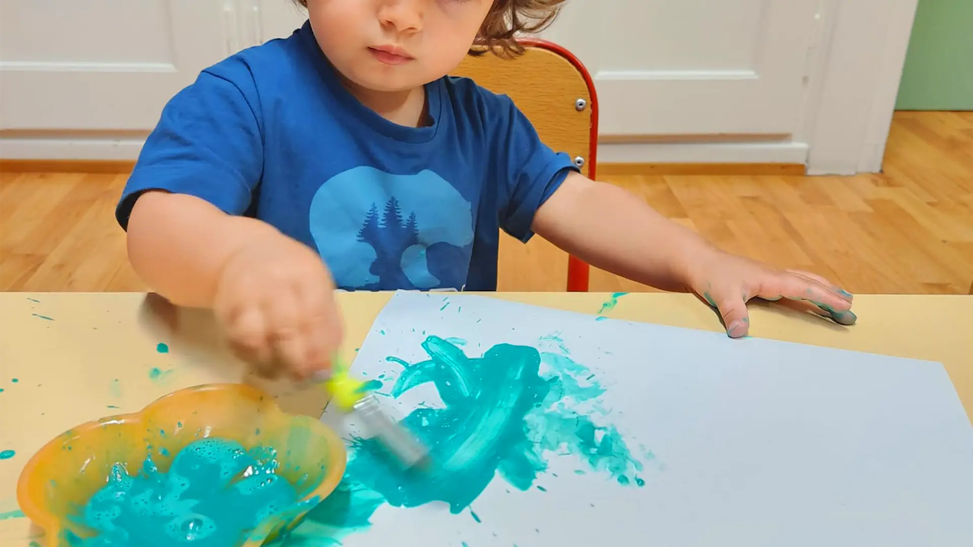 Enfant de la crèche Les Petits Acrobates soufflant dans une paille pour créer des bulles de peinture colorées sur une feuille à Lausanne.