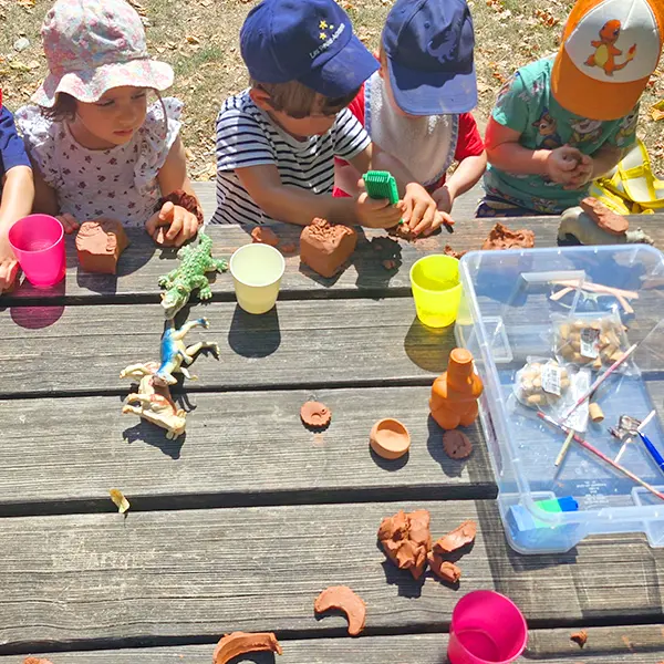 Groupe d’enfants façonnant la terre avec concentration pendant l’activité en plein air.