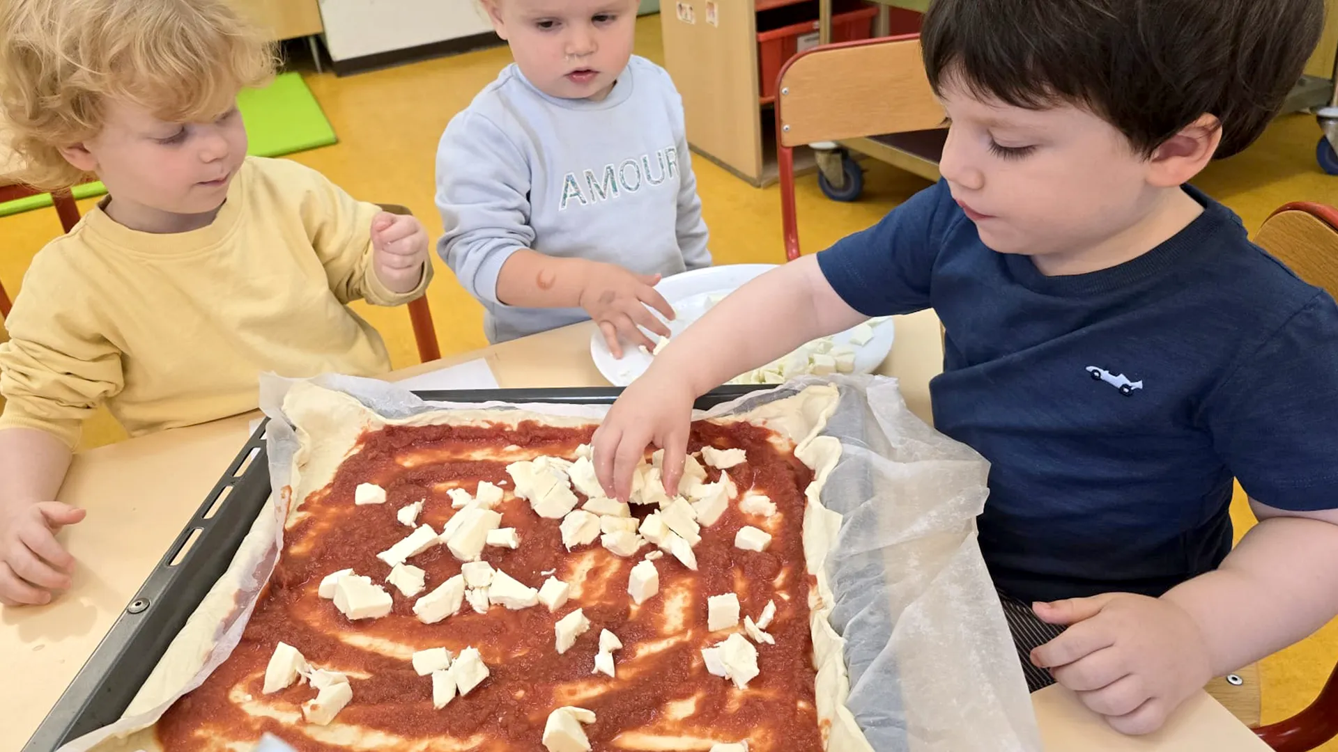 Enfants Trotteurs préparant une pizza maison avec leurs éducatrices.